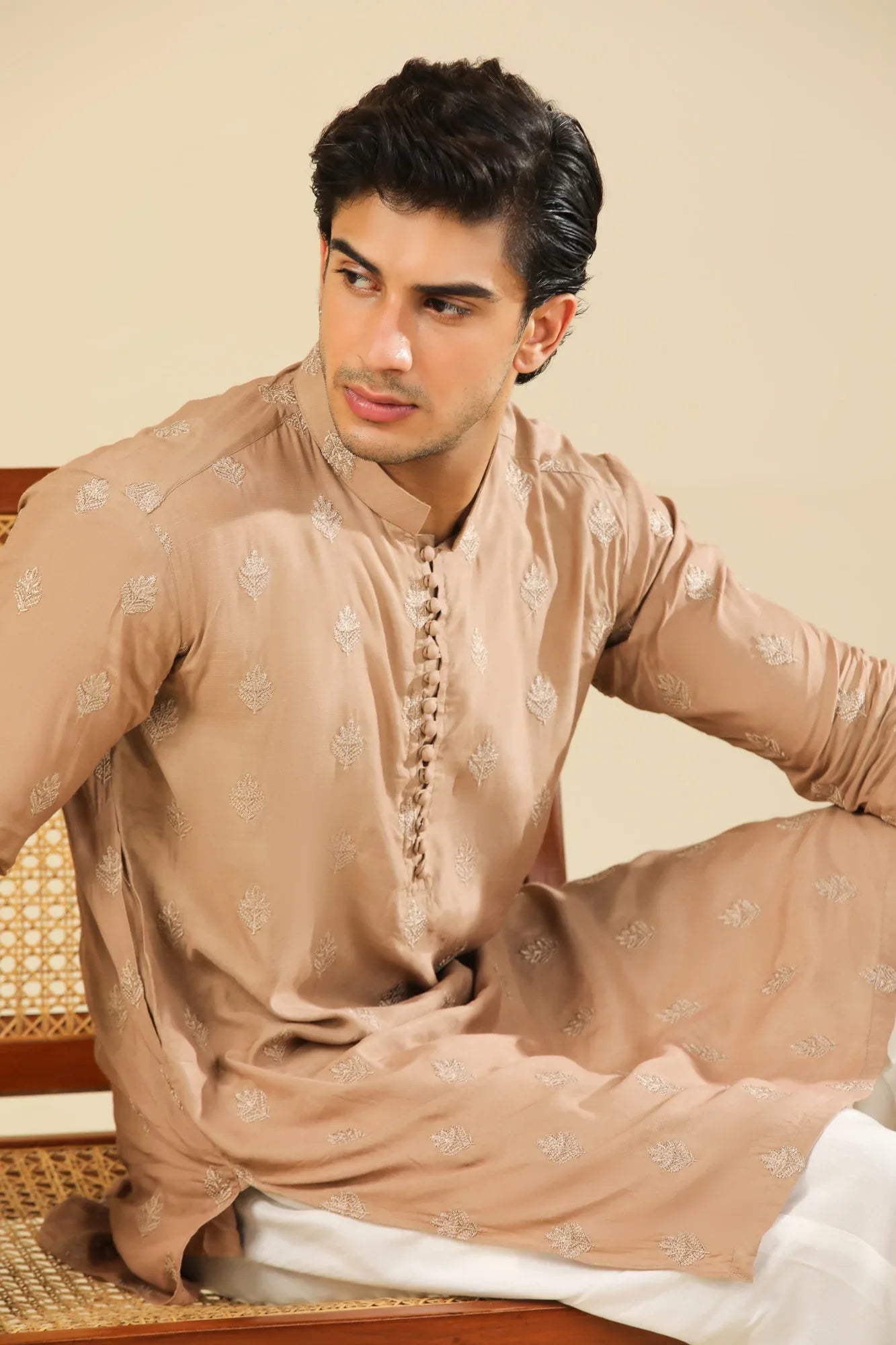 Man wearing a peach embroidered kurta and white trouser with a beige background
