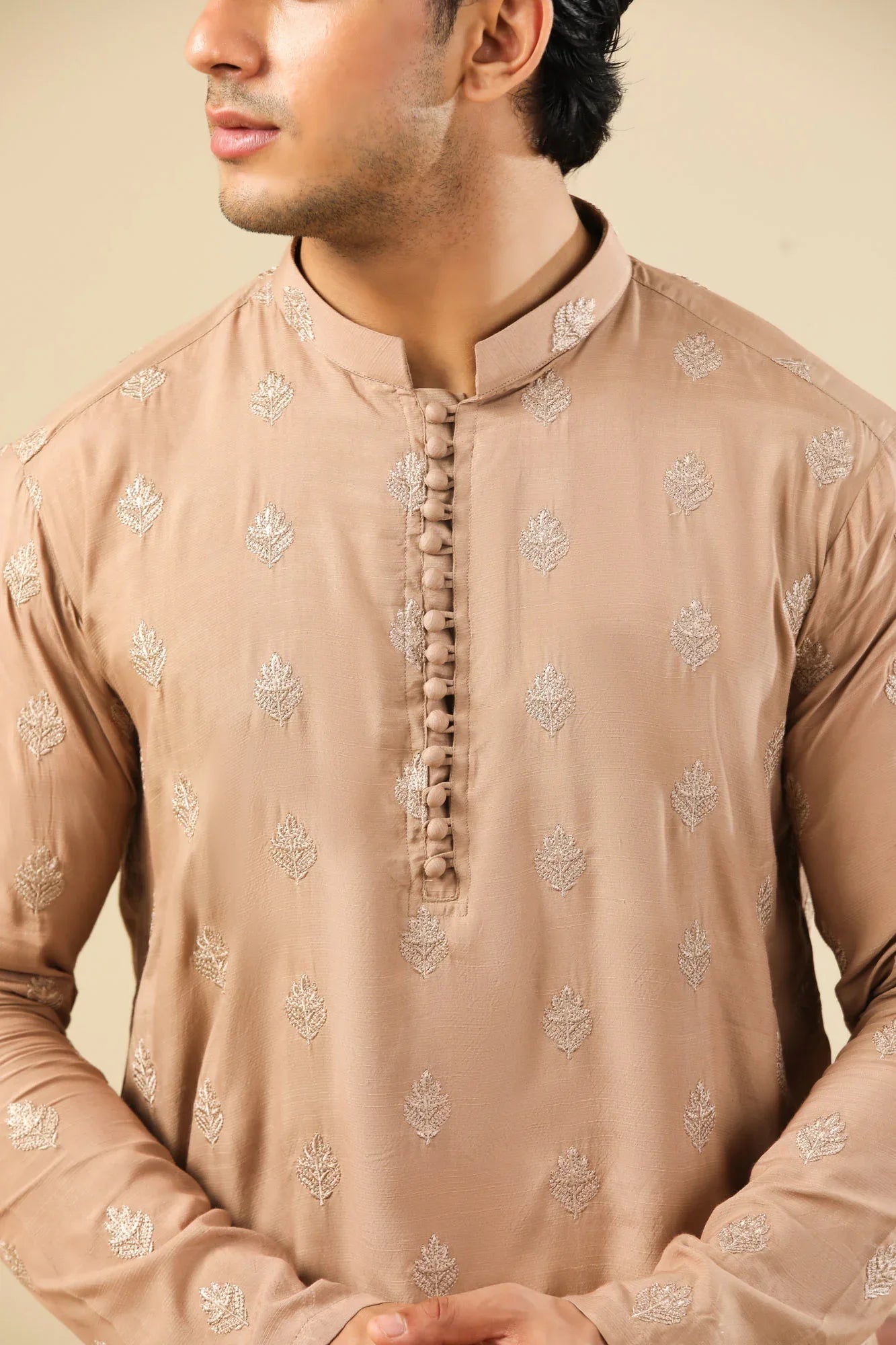 Man wearing a peach embroidered kurta and white trouser with a beige background