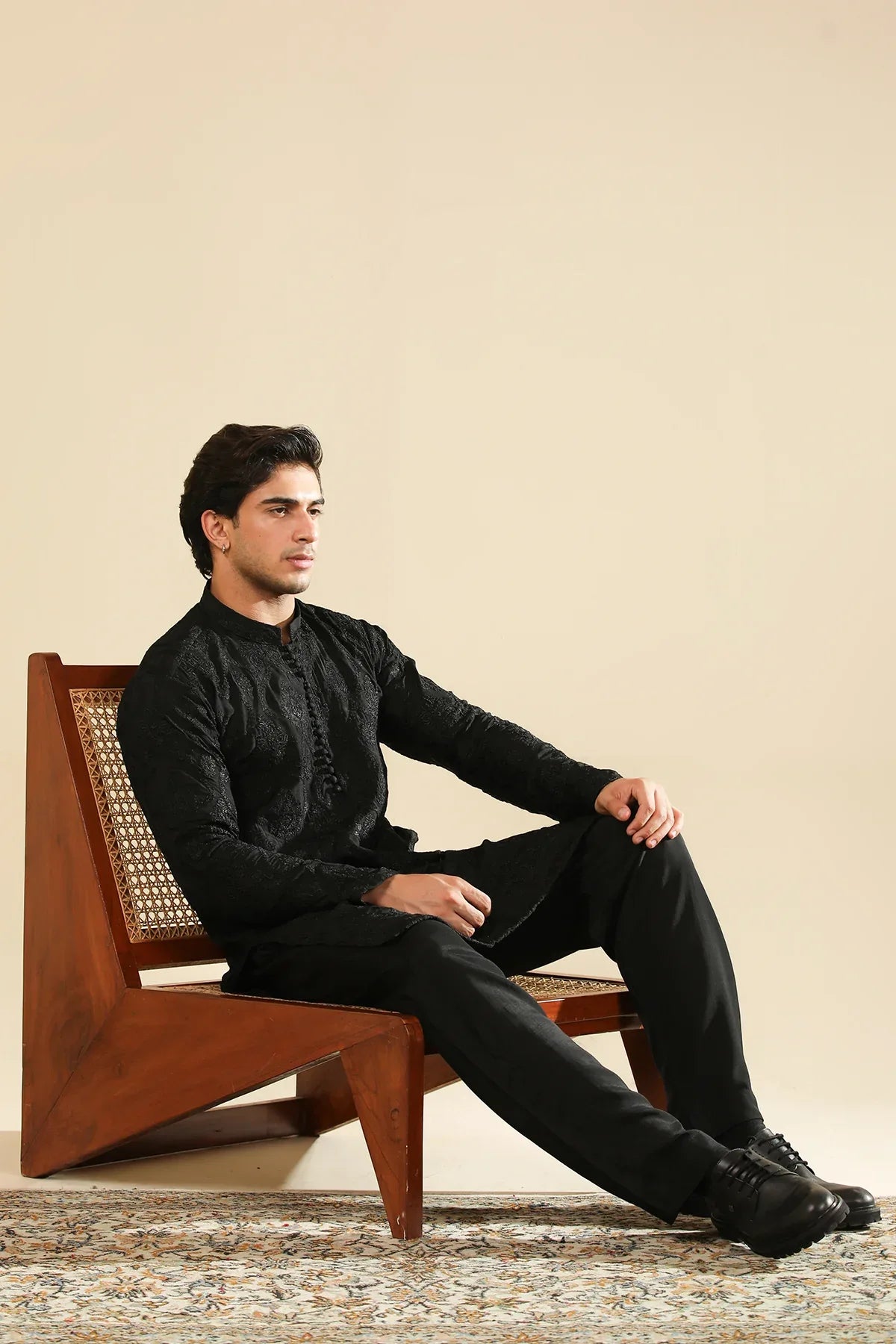 Man wearing a black raw silk embroidered kurta trouser against a beige background