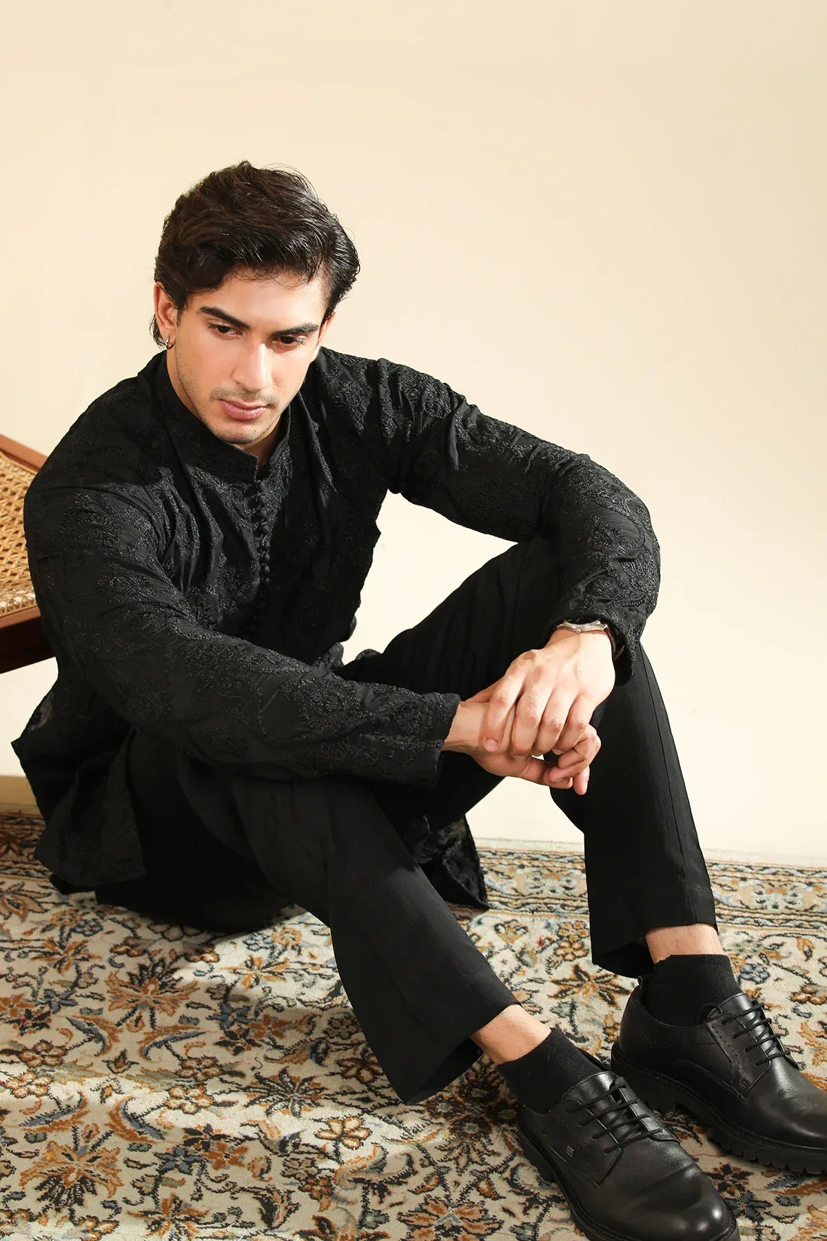 Man wearing a black raw silk embroidered kurta trouser against a beige background