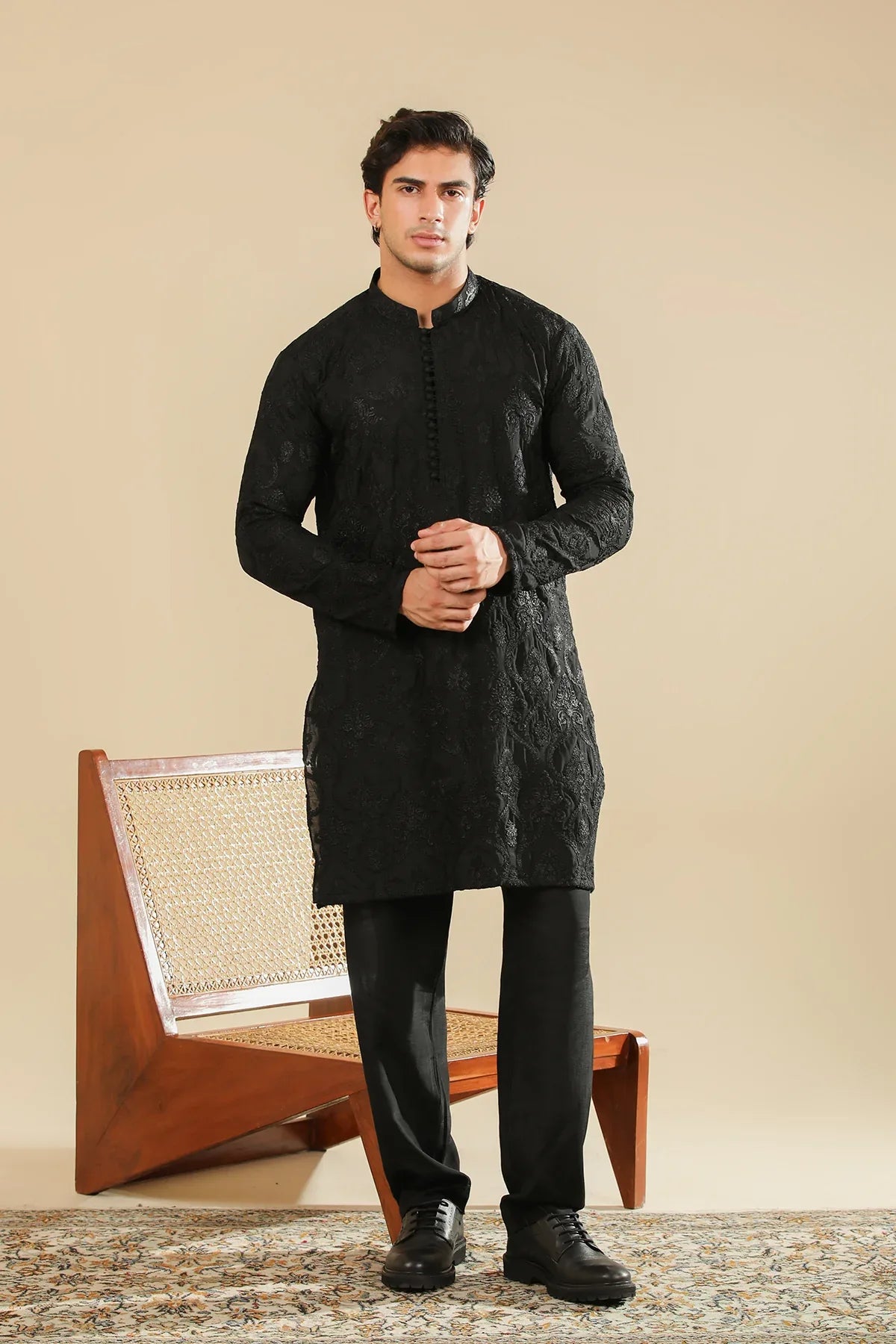 Man wearing a black raw silk embroidered kurta trouser against a beige background