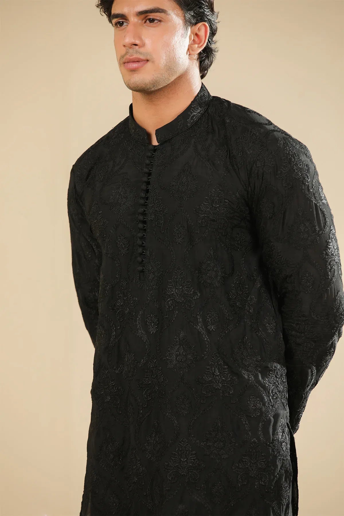 Man wearing a black raw silk embroidered kurta trouser against a beige background