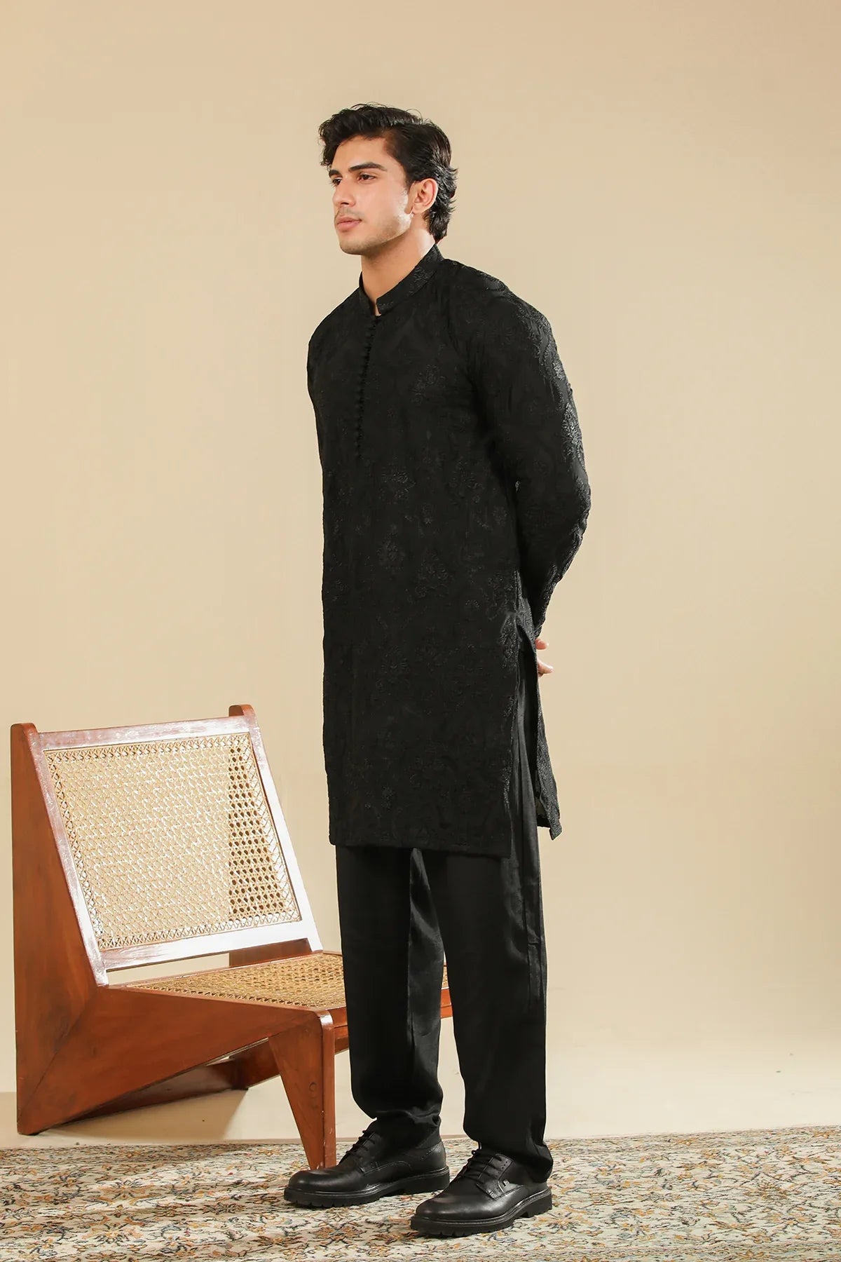 Man wearing a black raw silk embroidered kurta trouser against a beige background