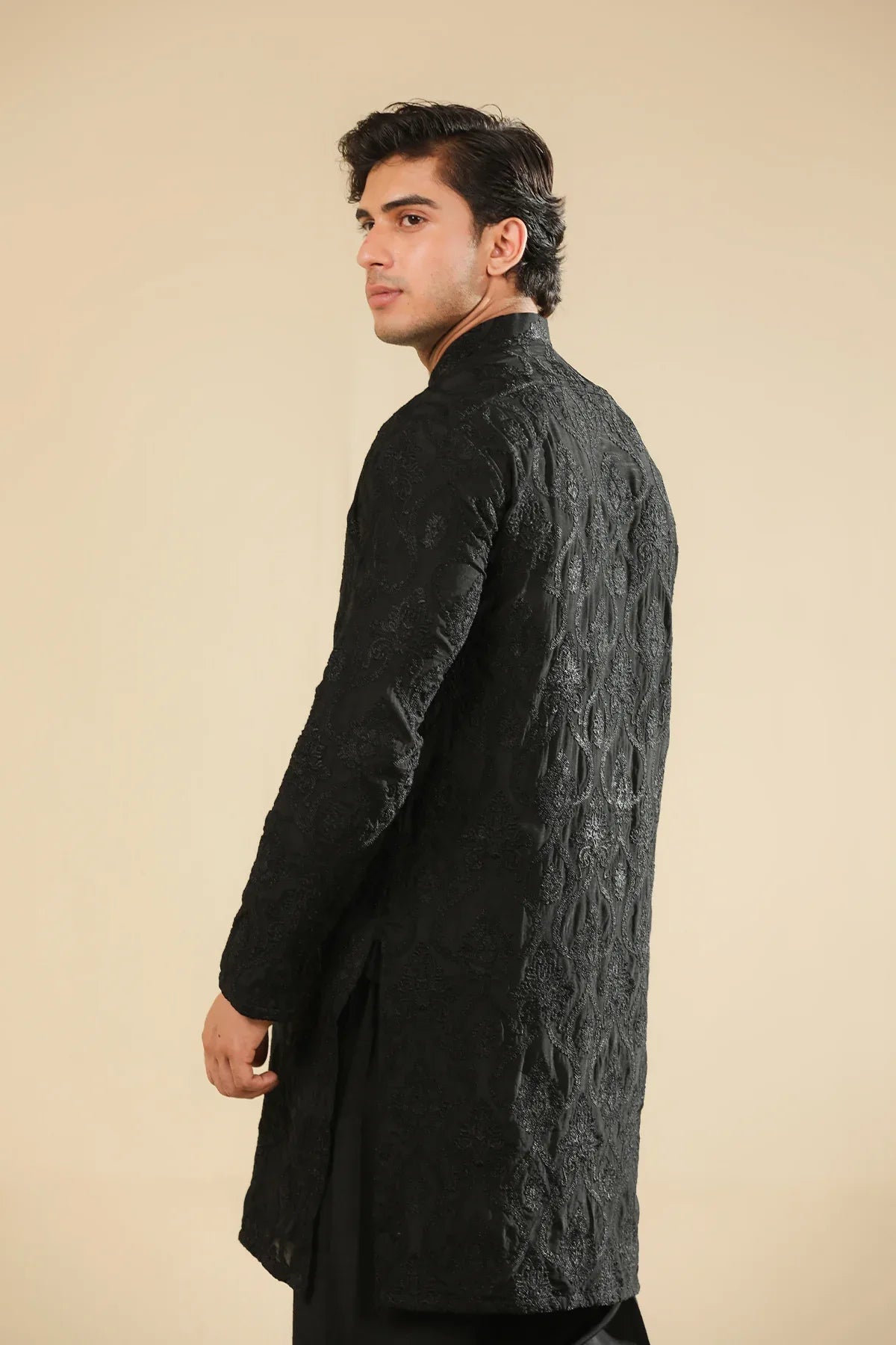 Man wearing a black raw silk embroidered kurta trouser against a beige background