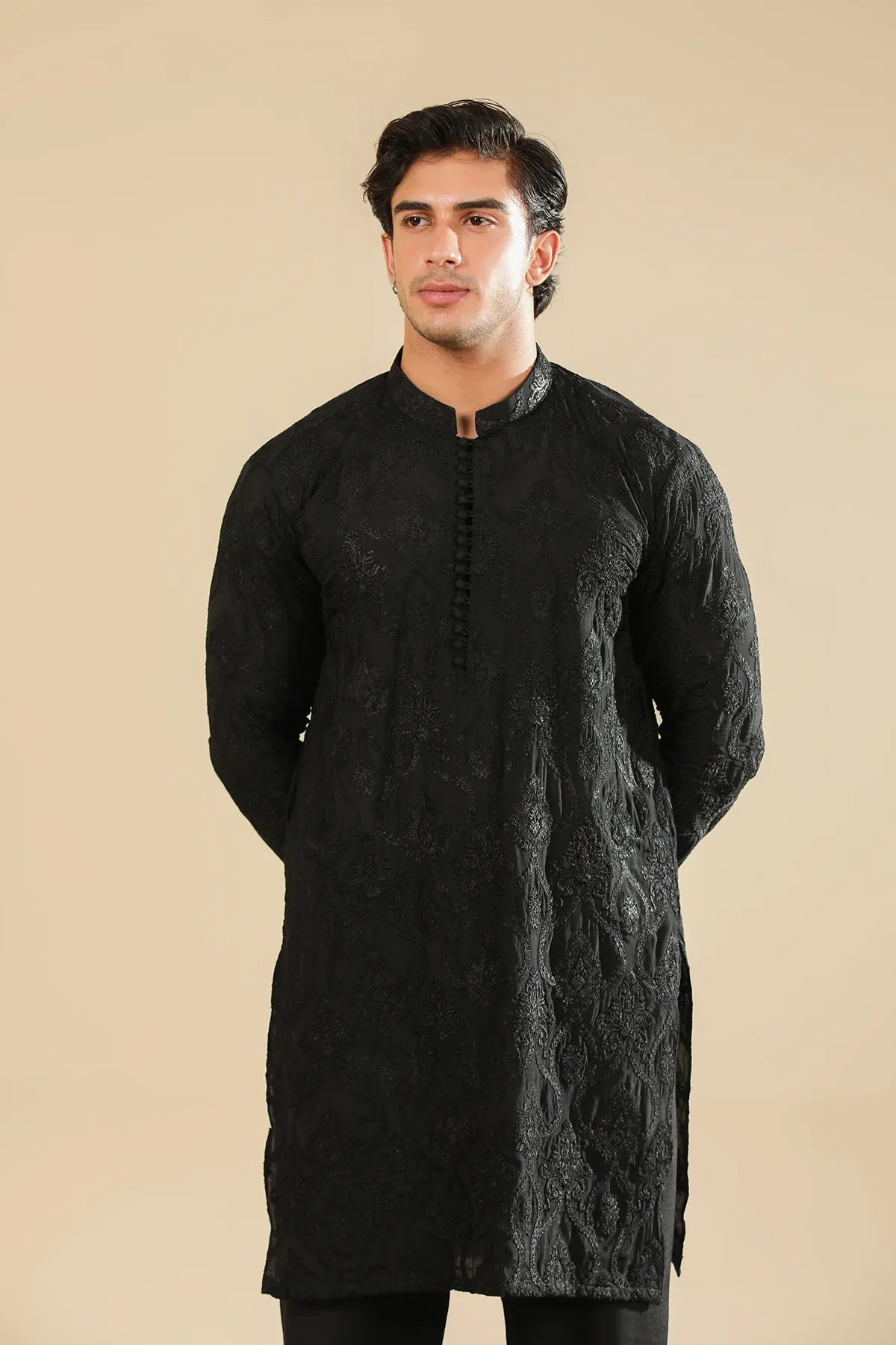 Man wearing a black raw silk embroidered kurta trouser against a beige background