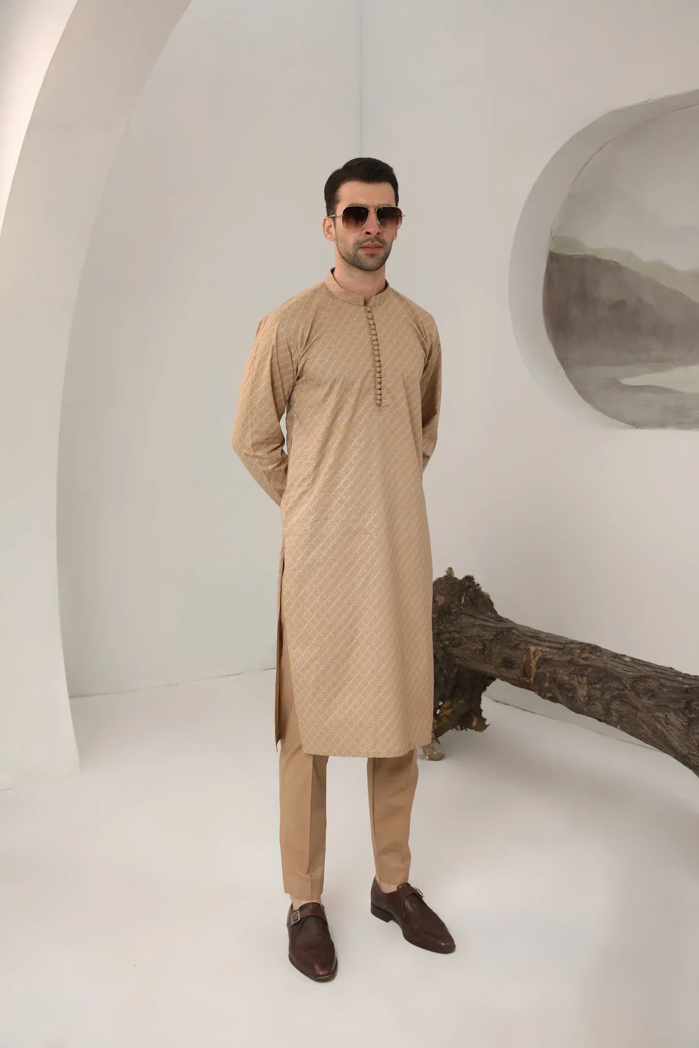 A man wearing a camel cotton embroidered kurta with full sleeves and a mandarin collar, paired with plain trousers.