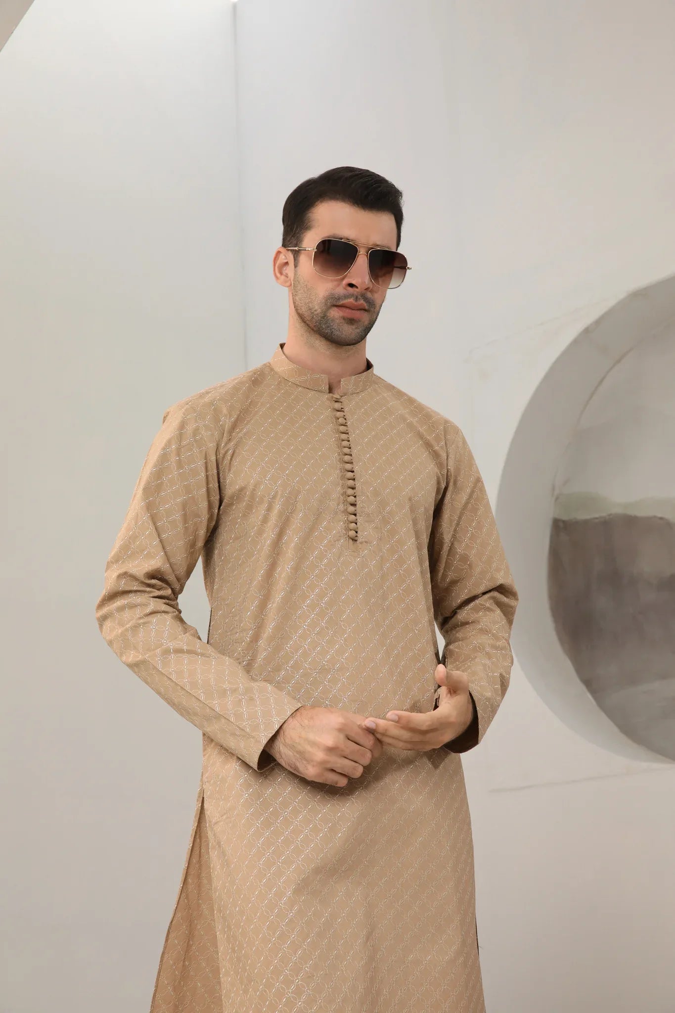 A man wearing a camel cotton embroidered kurta with full sleeves and a mandarin collar, paired with plain trousers.