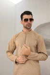 A man wearing a camel cotton embroidered kurta with full sleeves and a mandarin collar, paired with plain trousers.