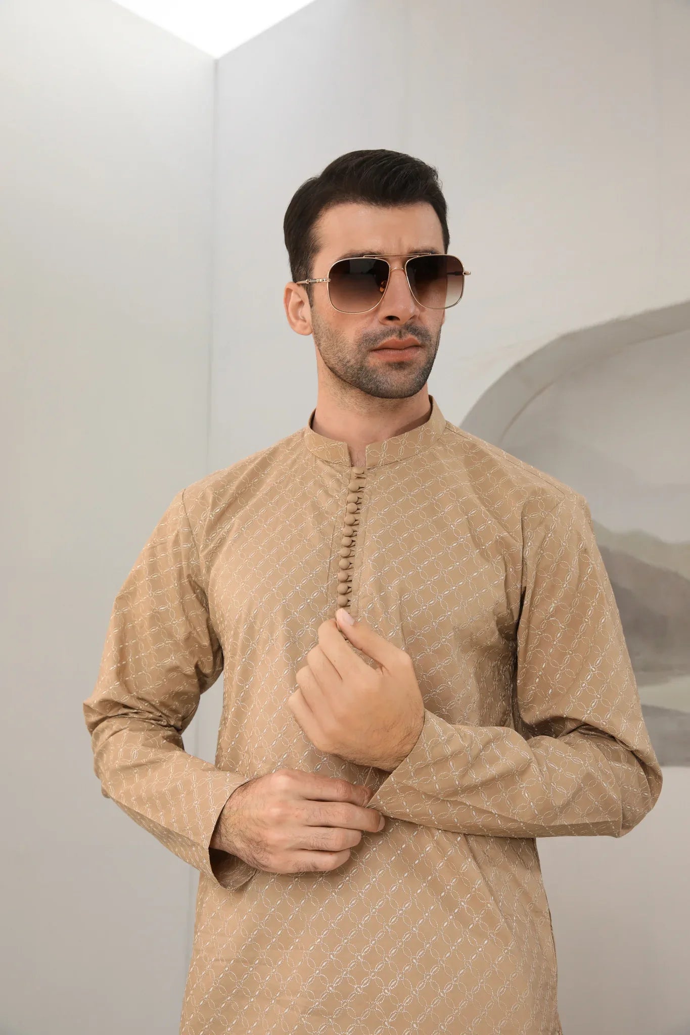A man wearing a camel cotton embroidered kurta with full sleeves and a mandarin collar, paired with plain trousers.