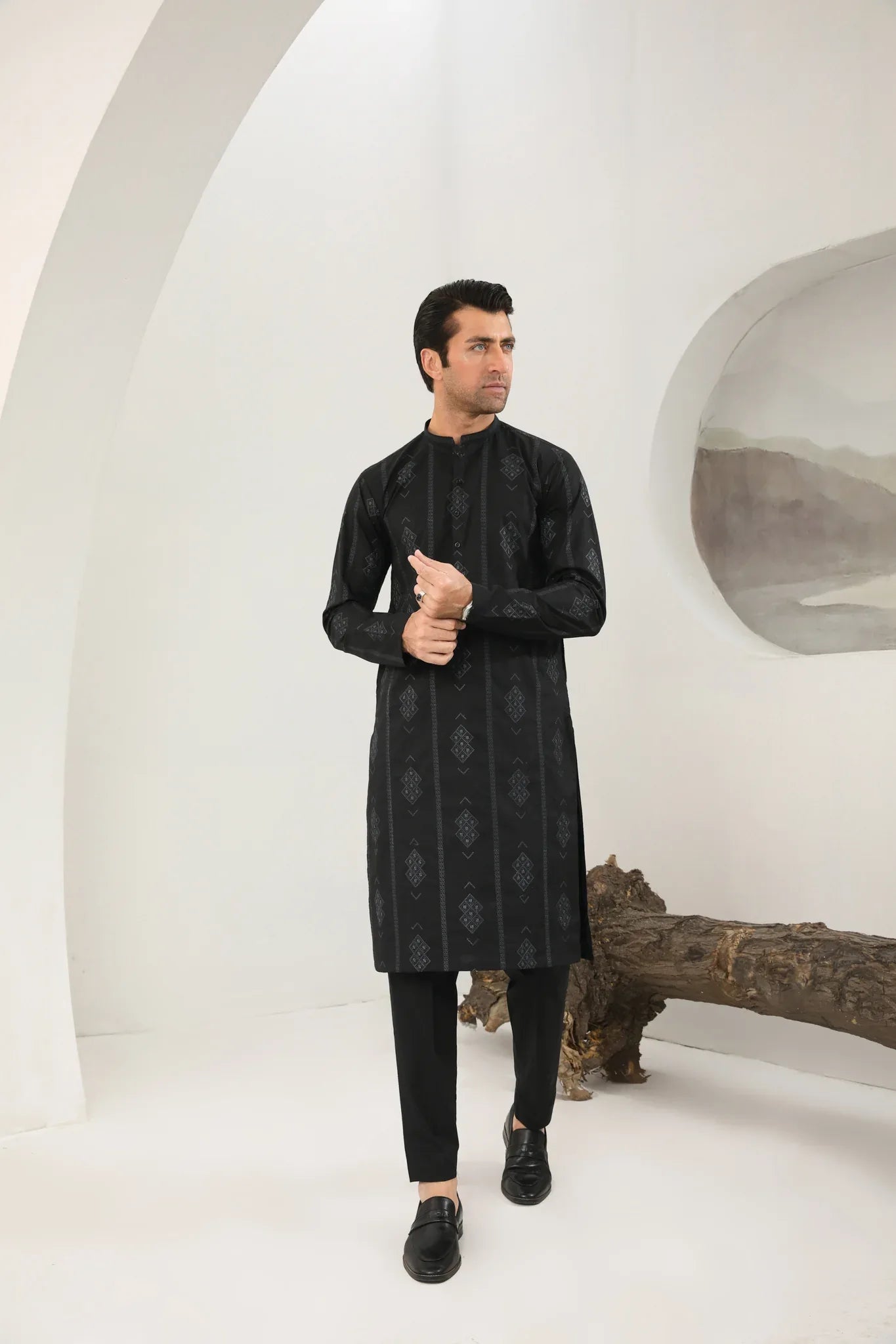 A man wearing a black embroidered kurta with full sleeves and a mandarin collar, paired with plain trousers.