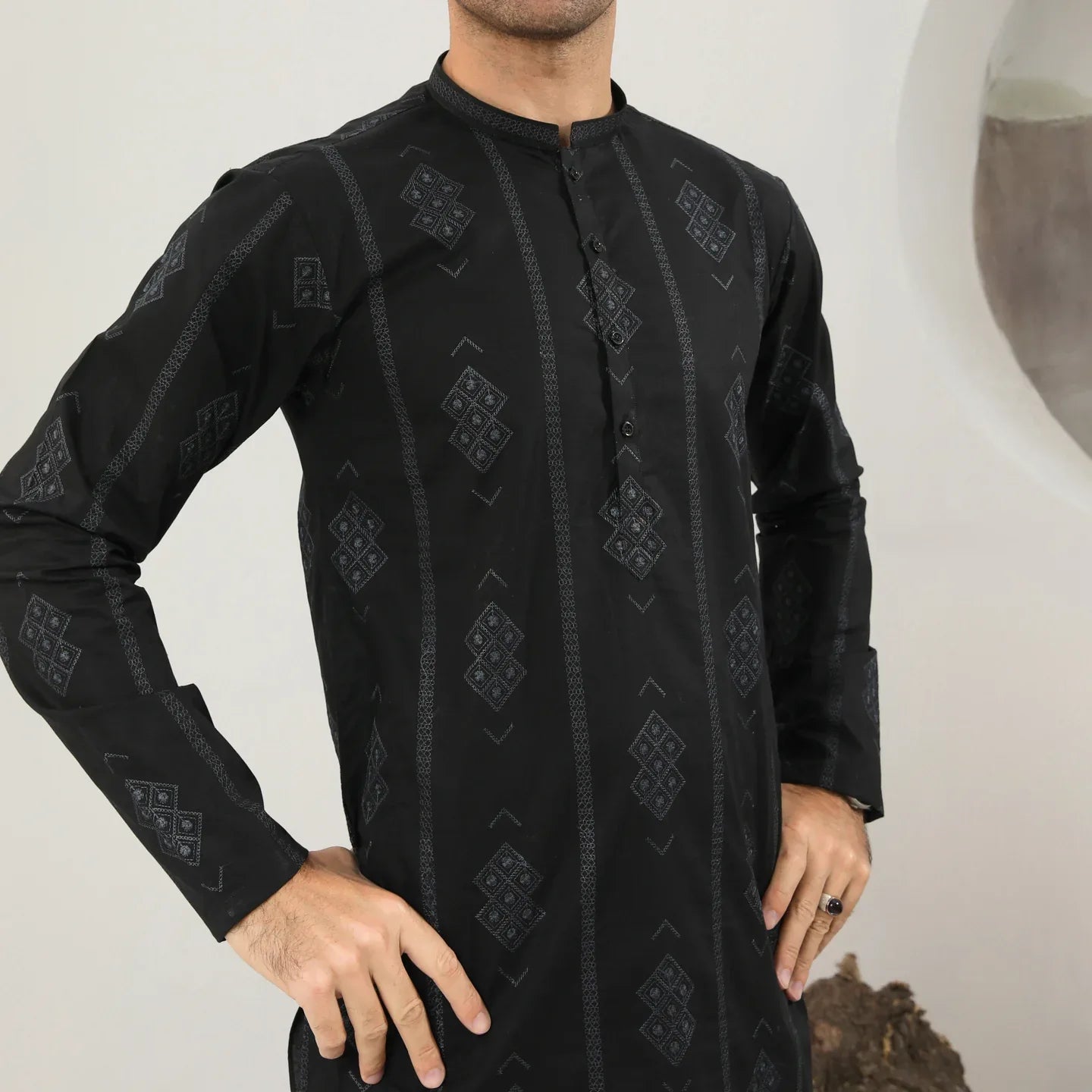A man wearing a black embroidered kurta with full sleeves and a mandarin collar, paired with plain trousers.