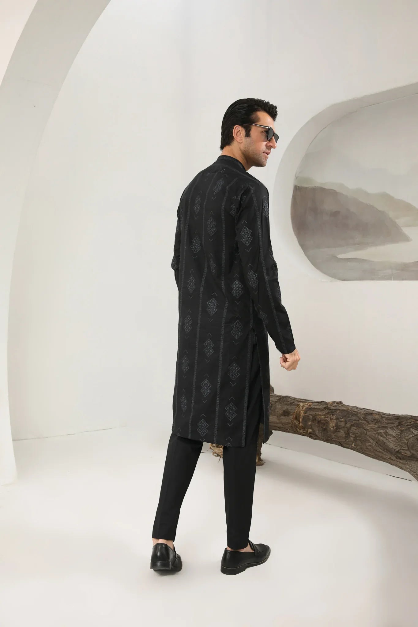 A man wearing a black embroidered kurta with full sleeves and a mandarin collar, paired with plain trousers.