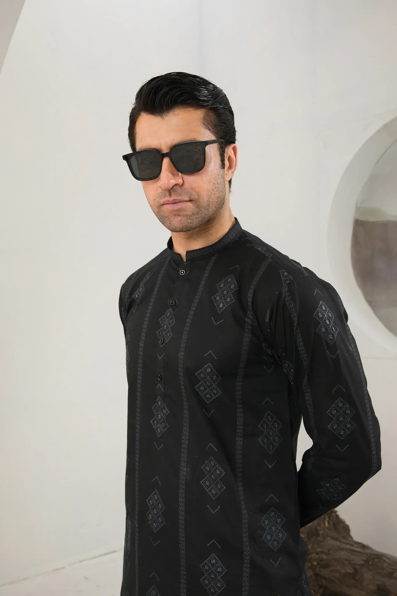 A man wearing a black embroidered kurta with full sleeves and a mandarin collar, paired with plain trousers.