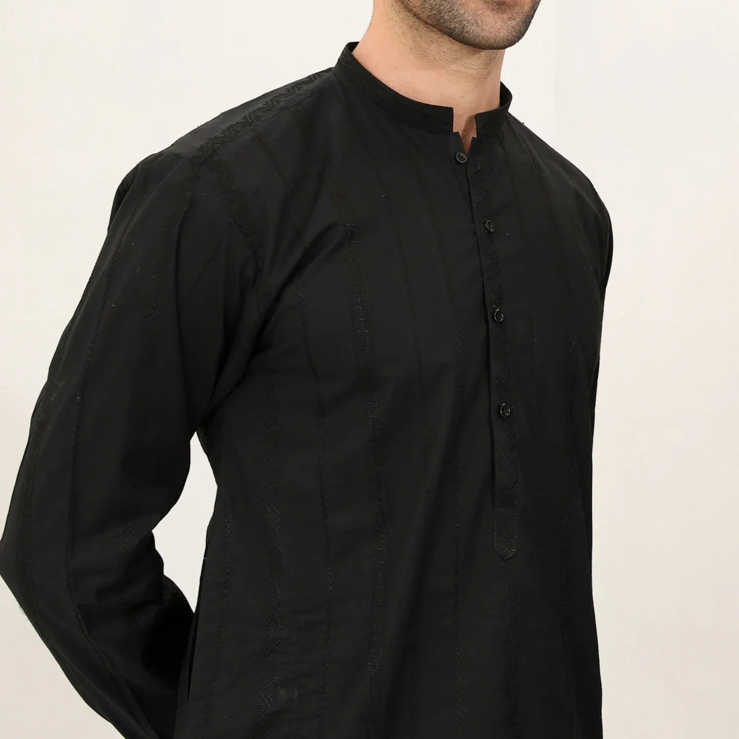 A man wearing a black embroidered kurta with full sleeves and a mandarin collar, paired with plain trousers.