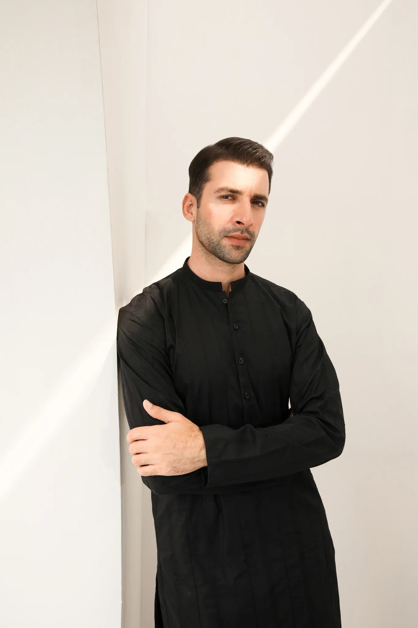 A man wearing a black embroidered kurta with full sleeves and a mandarin collar, paired with plain trousers.