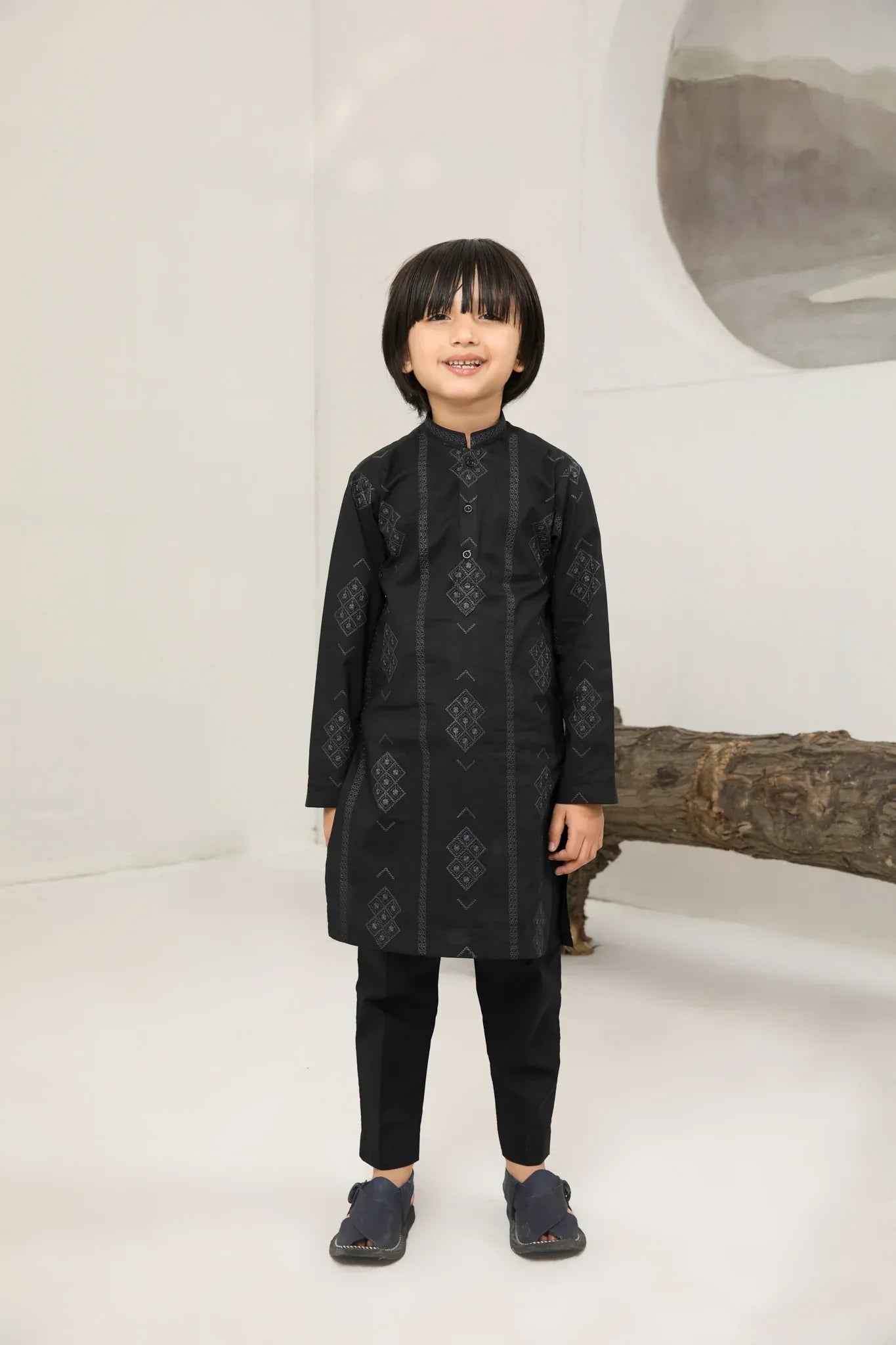 A child wearing a black cotton embroidered kurta trouser with a mandarin collar and full sleeves, standing in front of a plain background.