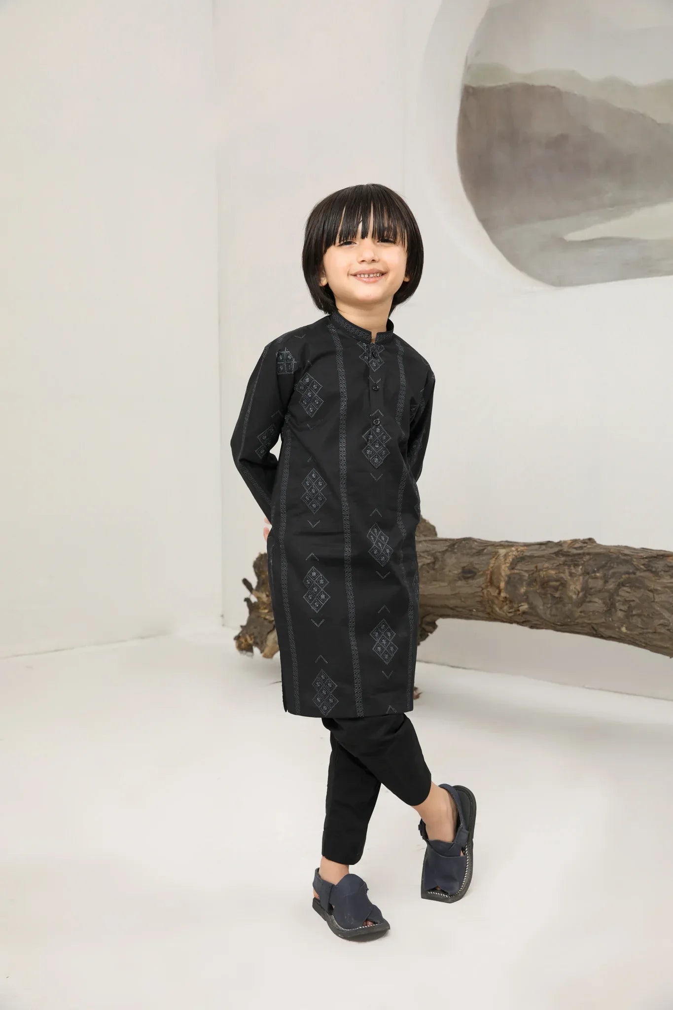 A child wearing a black cotton embroidered kurta trouser with a mandarin collar and full sleeves, standing in front of a plain background.