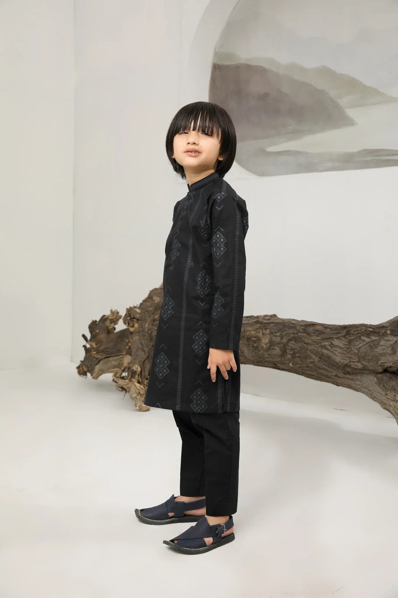 A child wearing a black cotton embroidered kurta trouser with a mandarin collar and full sleeves, standing in front of a plain background.