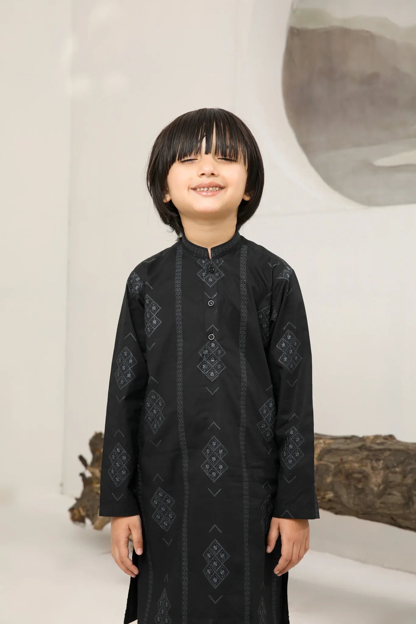 A child wearing a black cotton embroidered kurta trouser with a mandarin collar and full sleeves, standing in front of a plain background.