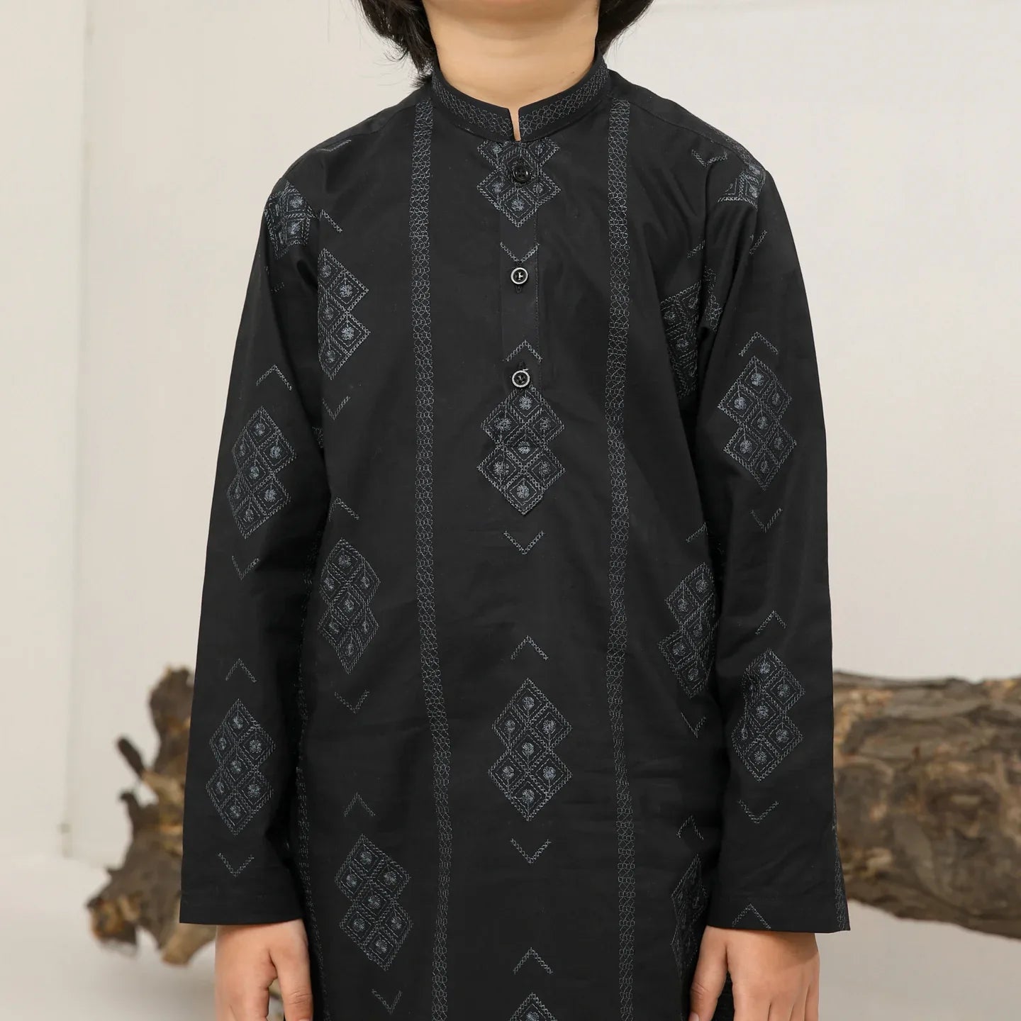 A child wearing a black cotton embroidered kurta trouser with a mandarin collar and full sleeves, standing in front of a plain background.