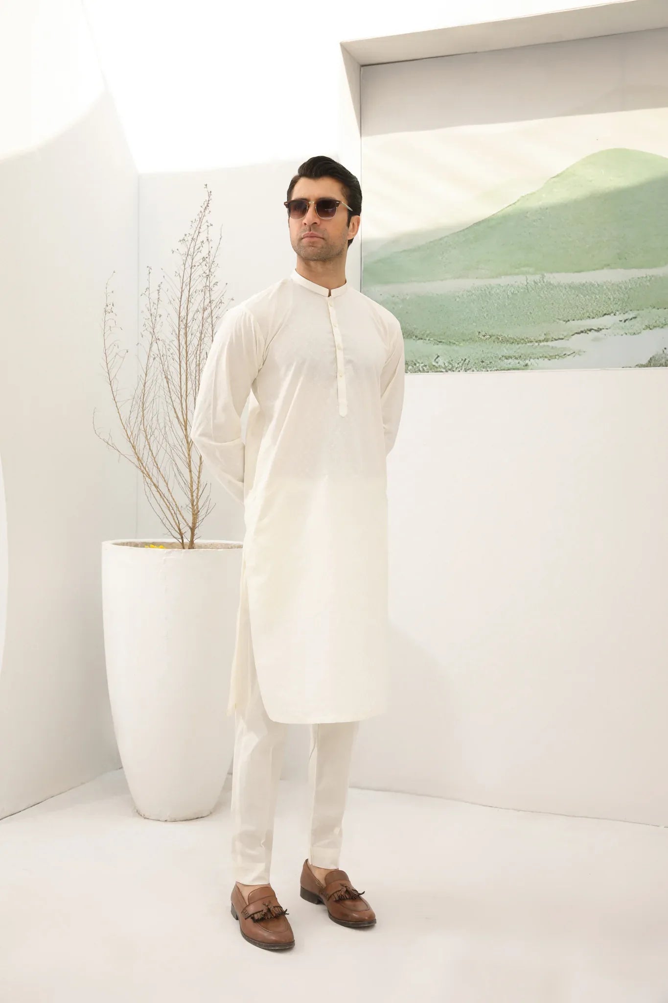 A man wearing a bsoky white cotton kurta embroidered with geometric patterns, featuring a mandarin collar and full sleeves, paired with plain trousers.