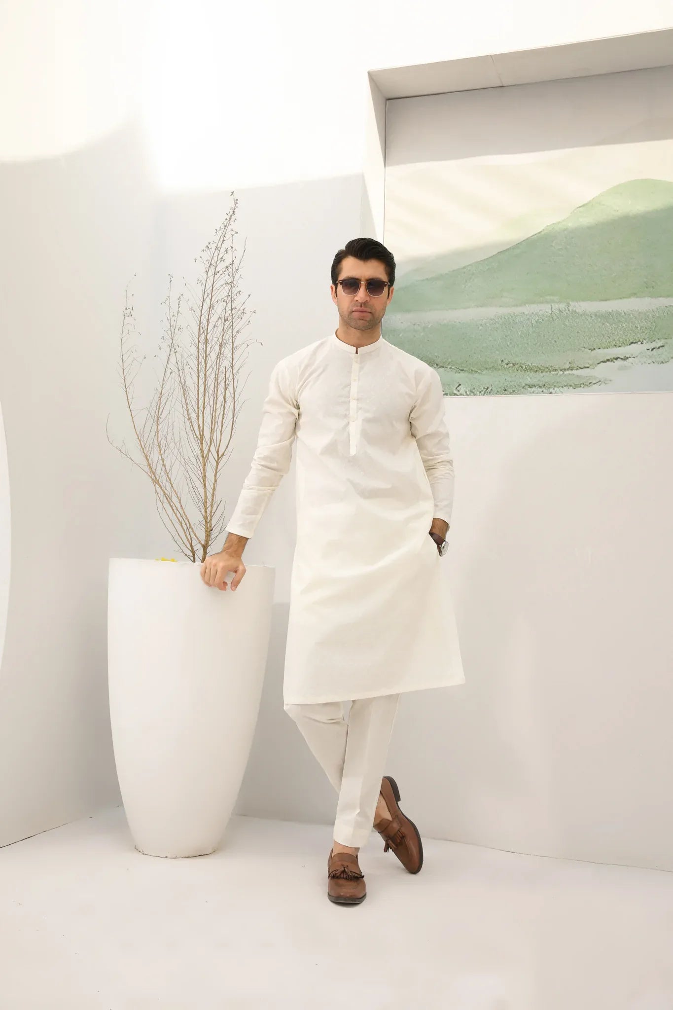 A man wearing a bsoky white cotton kurta embroidered with geometric patterns, featuring a mandarin collar and full sleeves, paired with plain trousers.