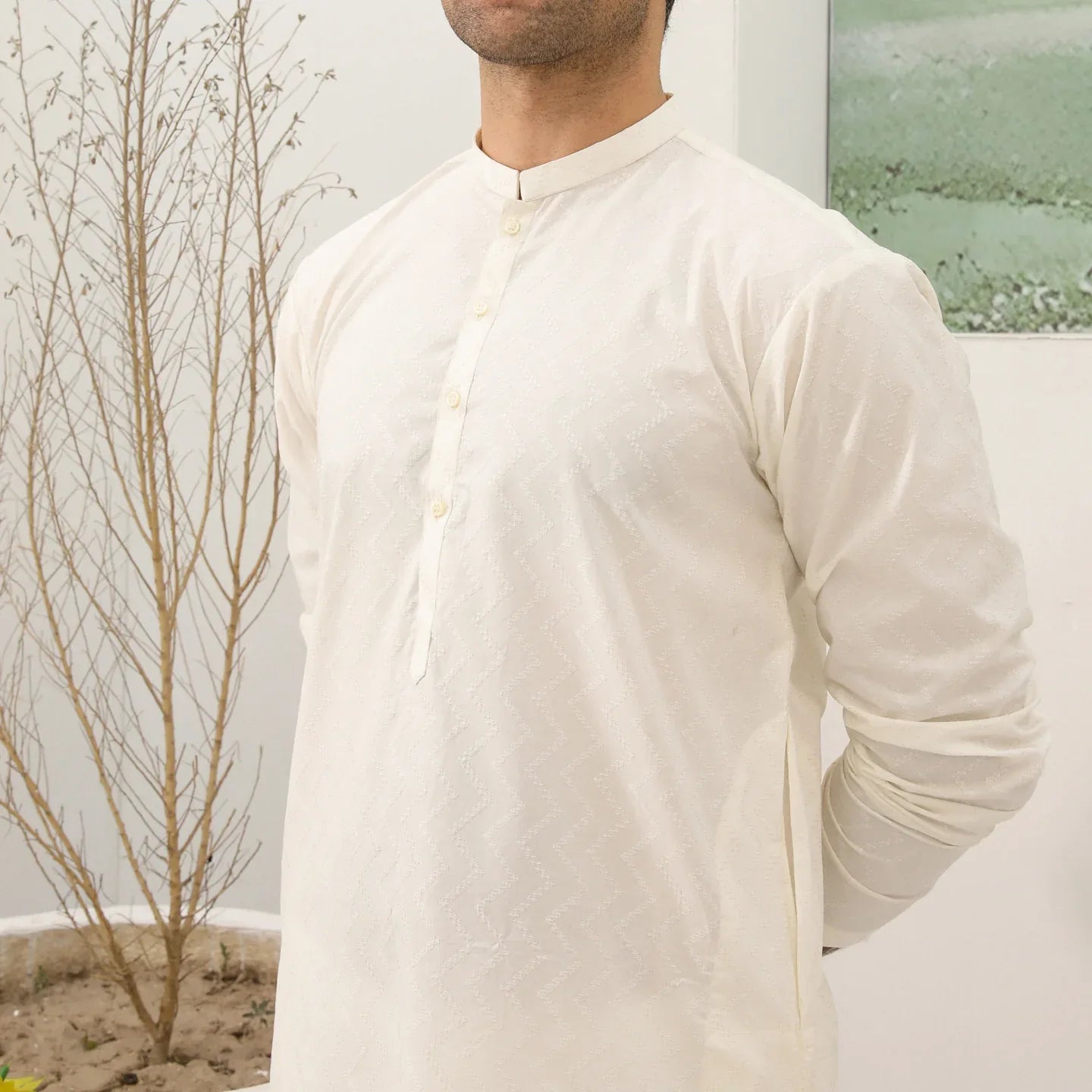 A man wearing a bsoky white cotton kurta embroidered with geometric patterns, featuring a mandarin collar and full sleeves, paired with plain trousers.
