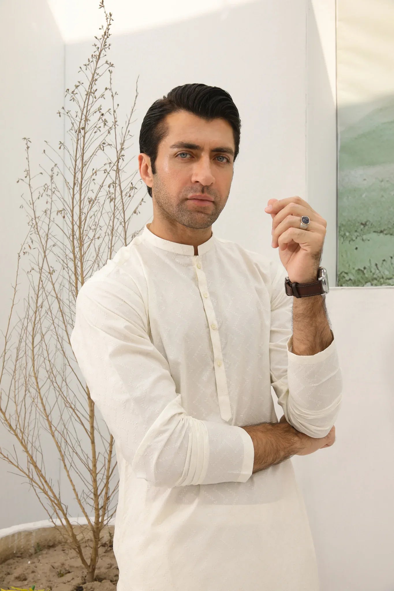 A man wearing a bsoky white cotton kurta embroidered with geometric patterns, featuring a mandarin collar and full sleeves, paired with plain trousers.
