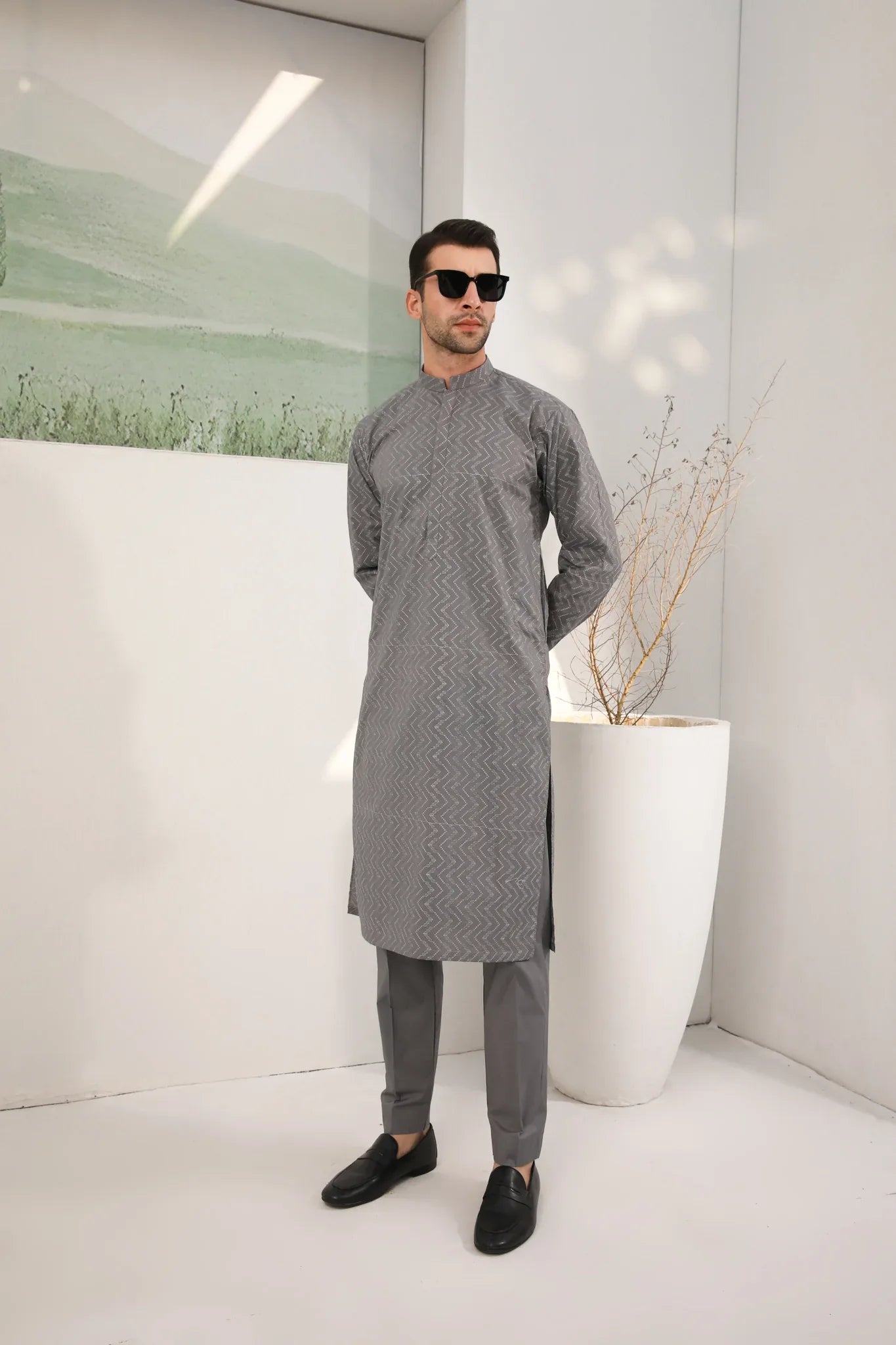 A man wearing a light grey embroidered kurta with full sleeves and a mandarin collar, paired with a plain trouser.