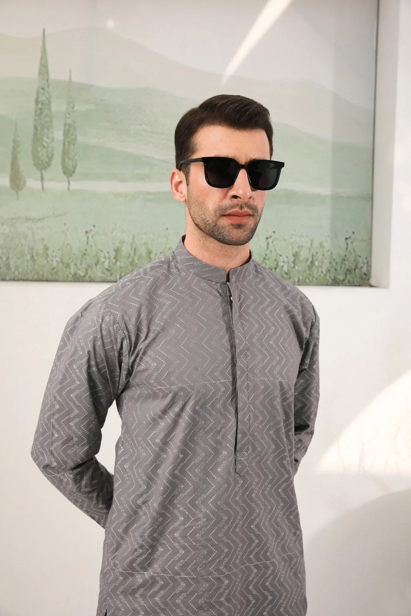 A man wearing a light grey embroidered kurta with full sleeves and a mandarin collar, paired with a plain trouser.