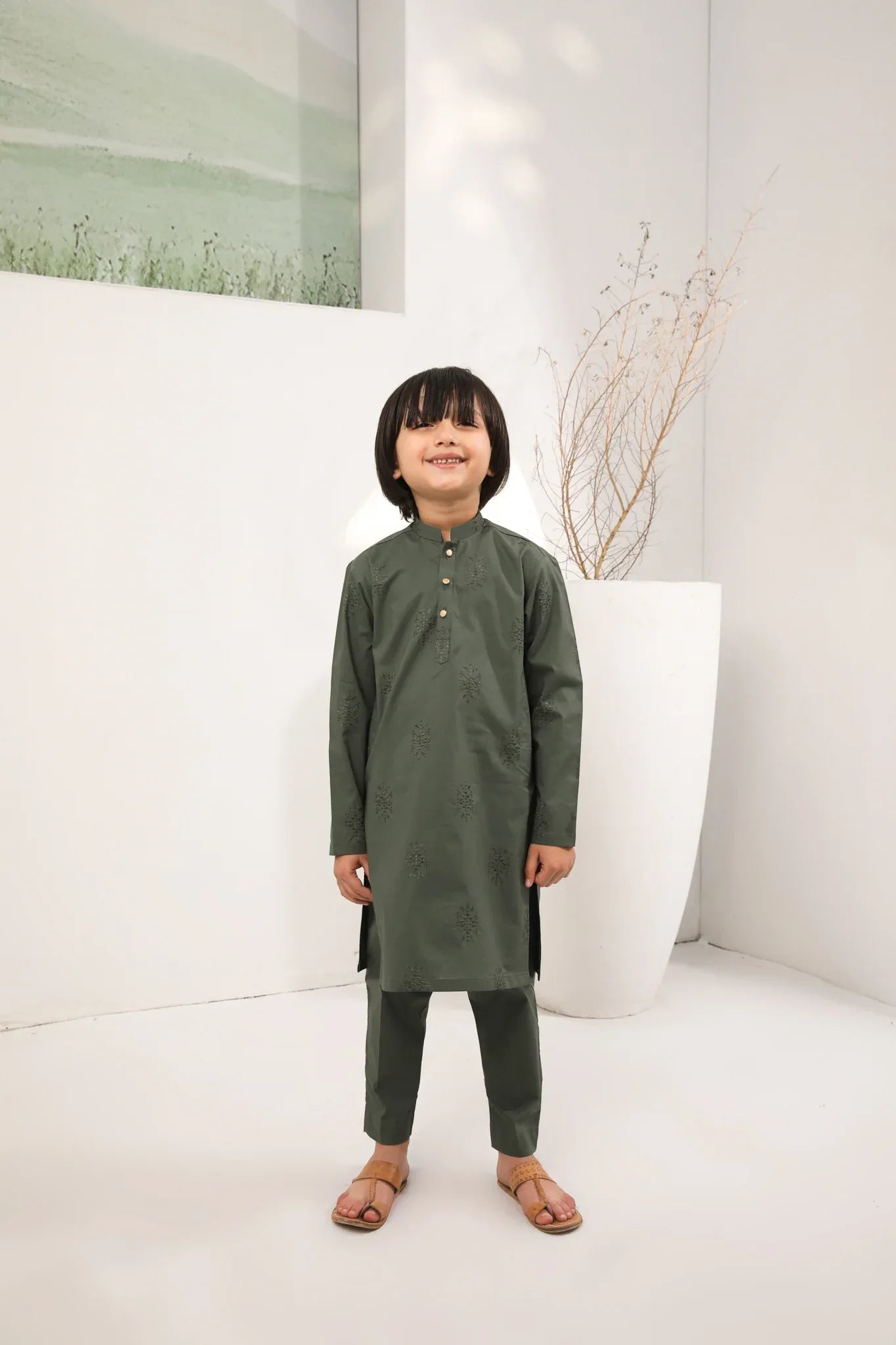 A child standing wearing an army green cotton embroidered kurta with full sleeves and a mandarin collar, paired with plain cotton trousers.