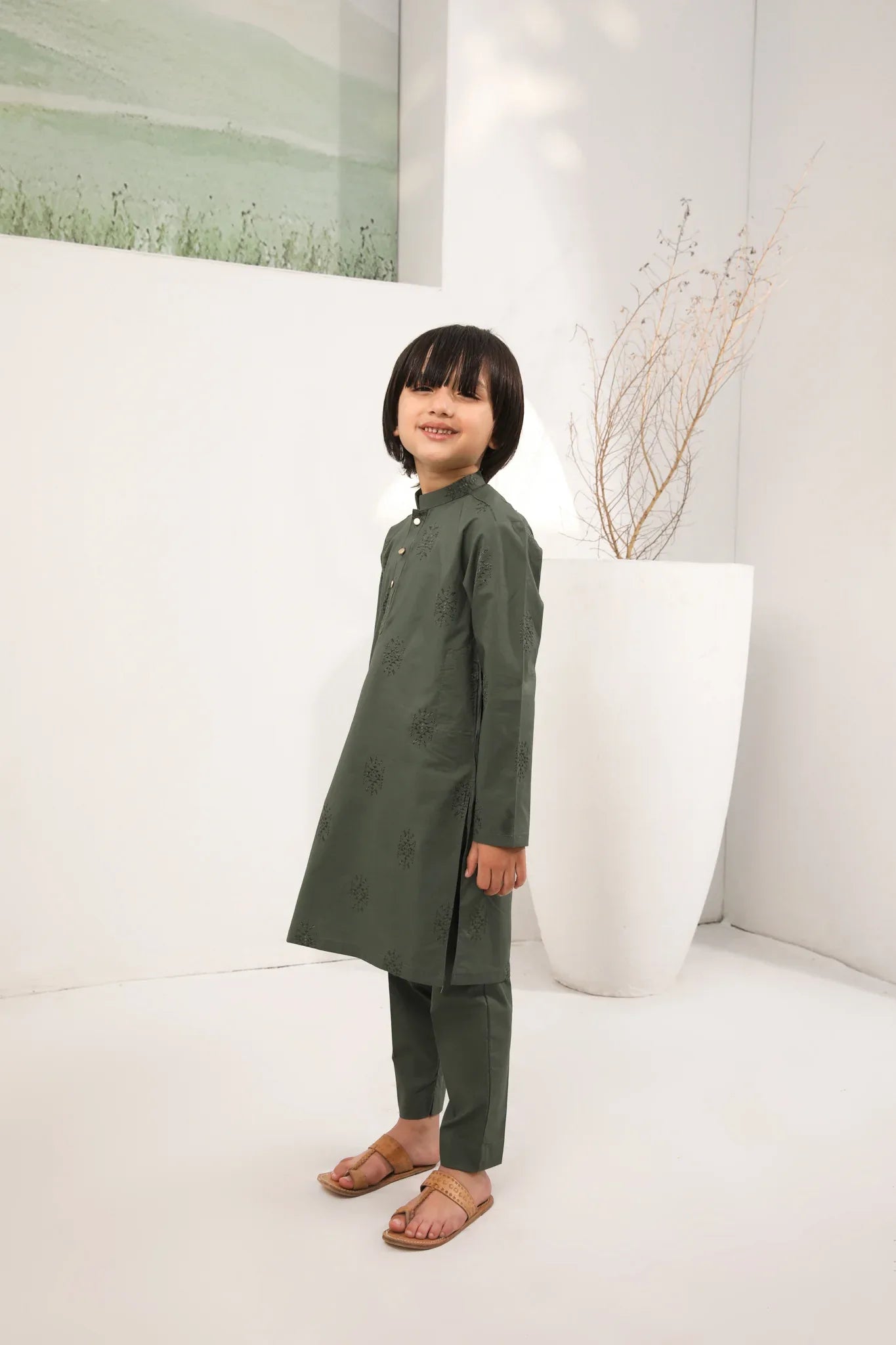 A child standing wearing an army green cotton embroidered kurta with full sleeves and a mandarin collar, paired with plain cotton trousers.
