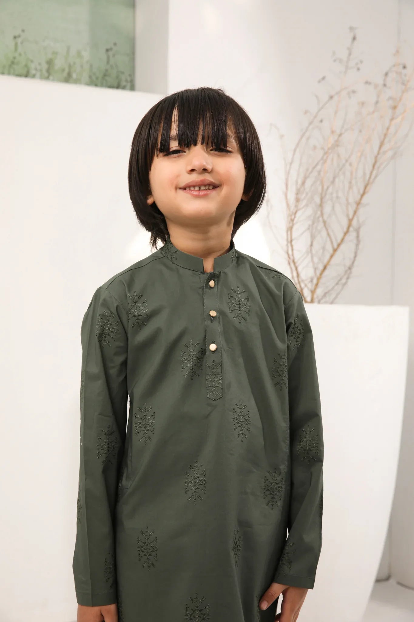 A child standing wearing an army green cotton embroidered kurta with full sleeves and a mandarin collar, paired with plain cotton trousers.