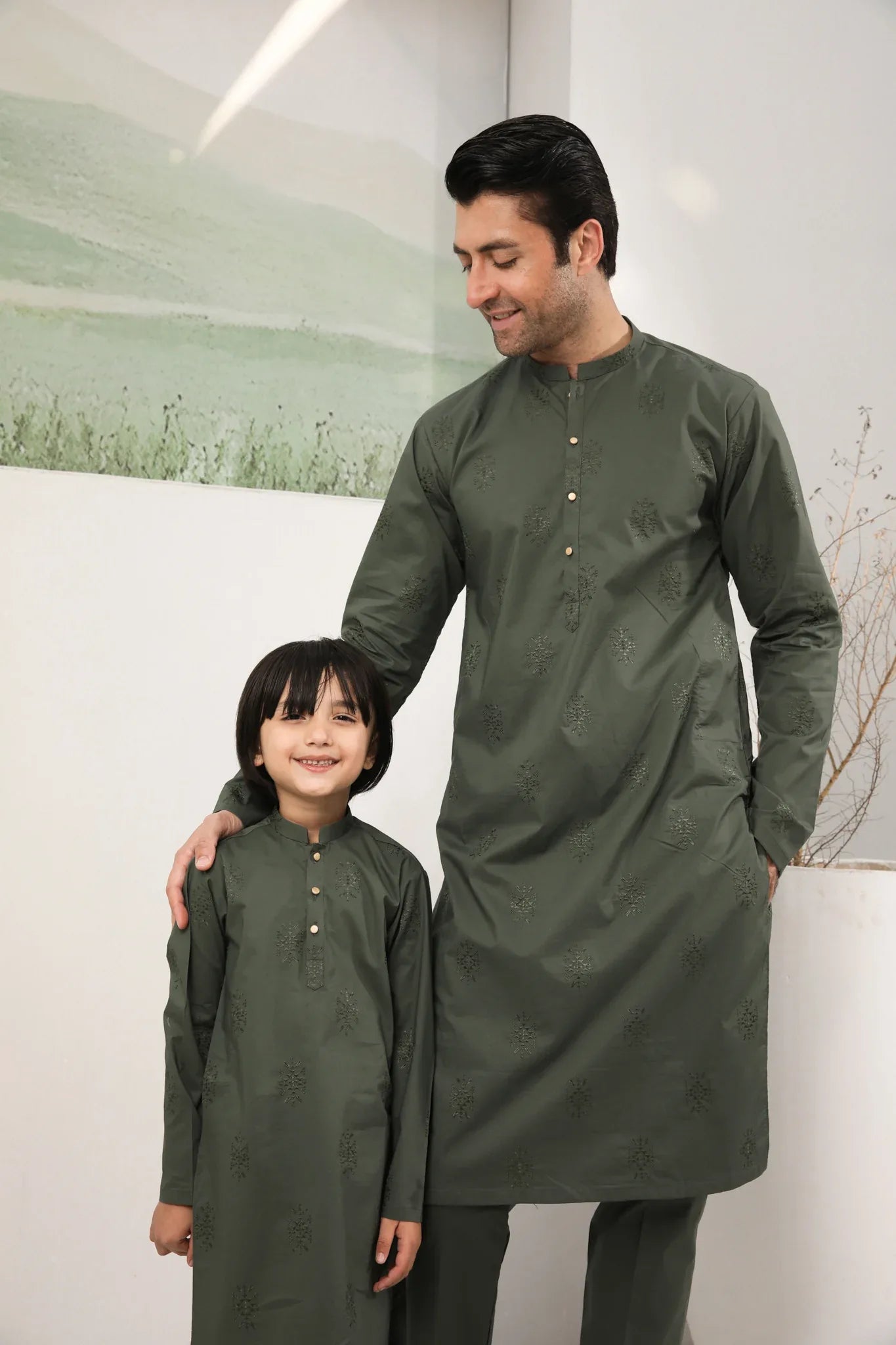A man standing against a backdrop wearing a army green emnroidered kurta trouser.