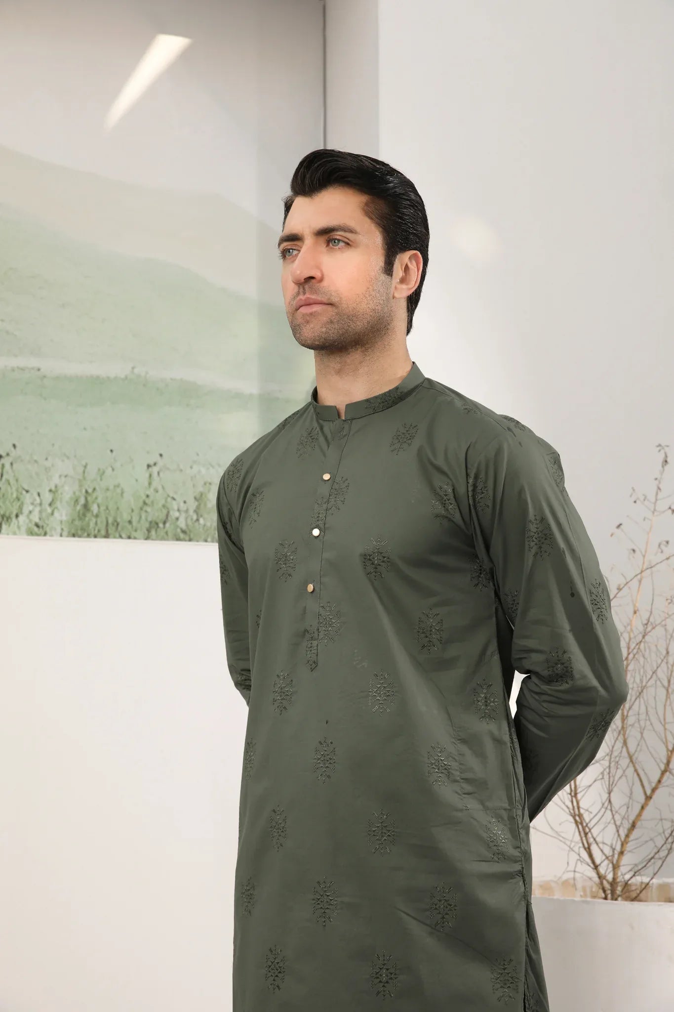 A man standing against a backdrop wearing a army green emnroidered kurta trouser.
