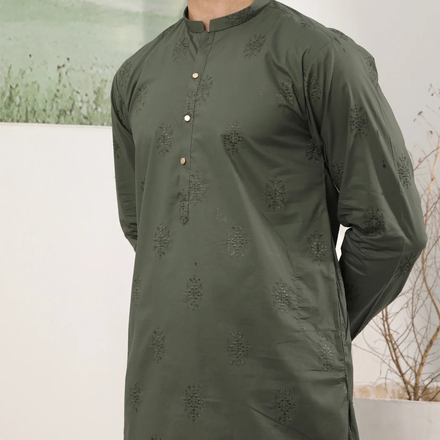 A man standing against a backdrop wearing a army green emnroidered kurta trouser.