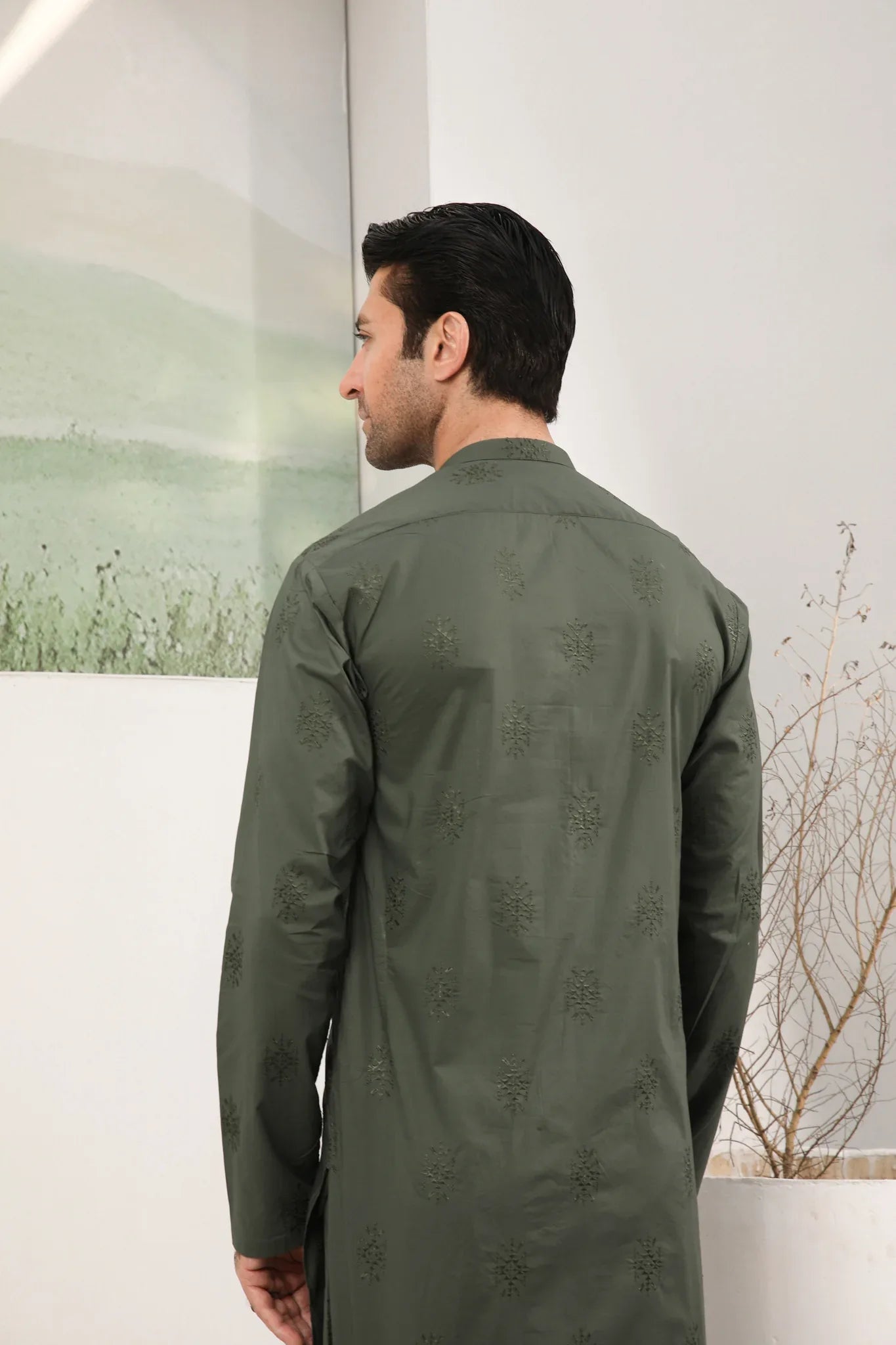 A man standing against a backdrop wearing a army green emnroidered kurta trouser.