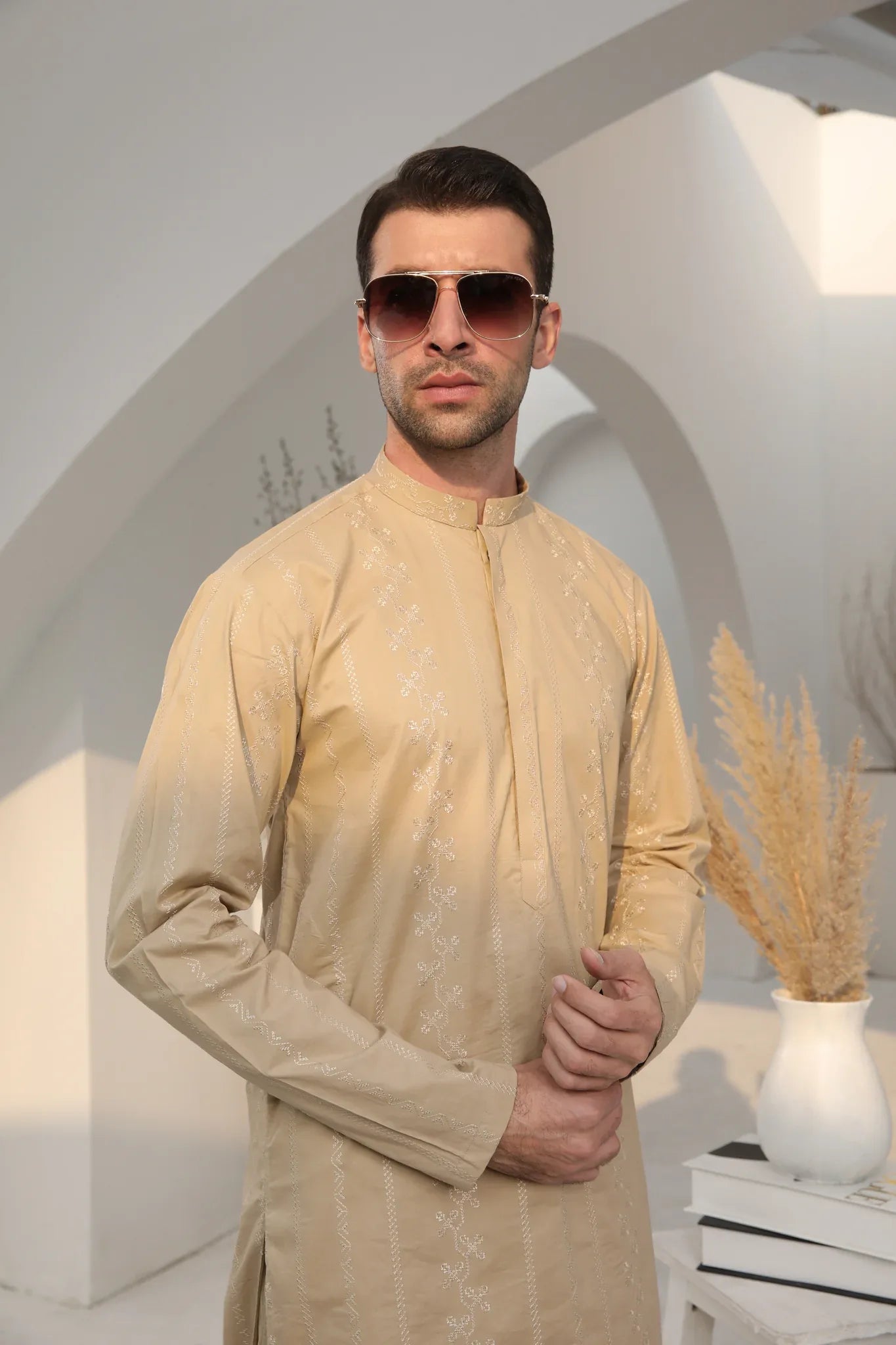 A man wearing a beige embroidered kurta with full sleeves and a mandarin collar, paired with a plain trouser.