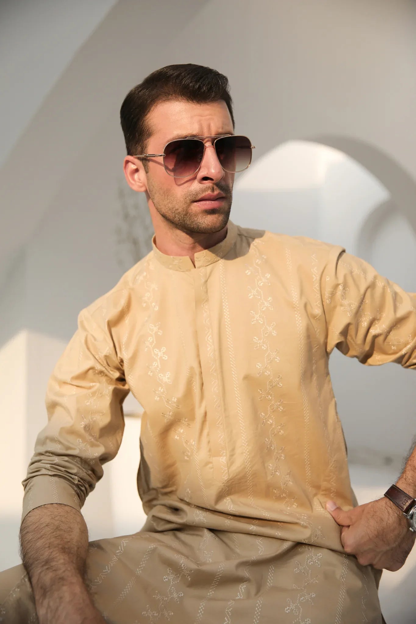 A man wearing a beige embroidered kurta with full sleeves and a mandarin collar, paired with a plain trouser.