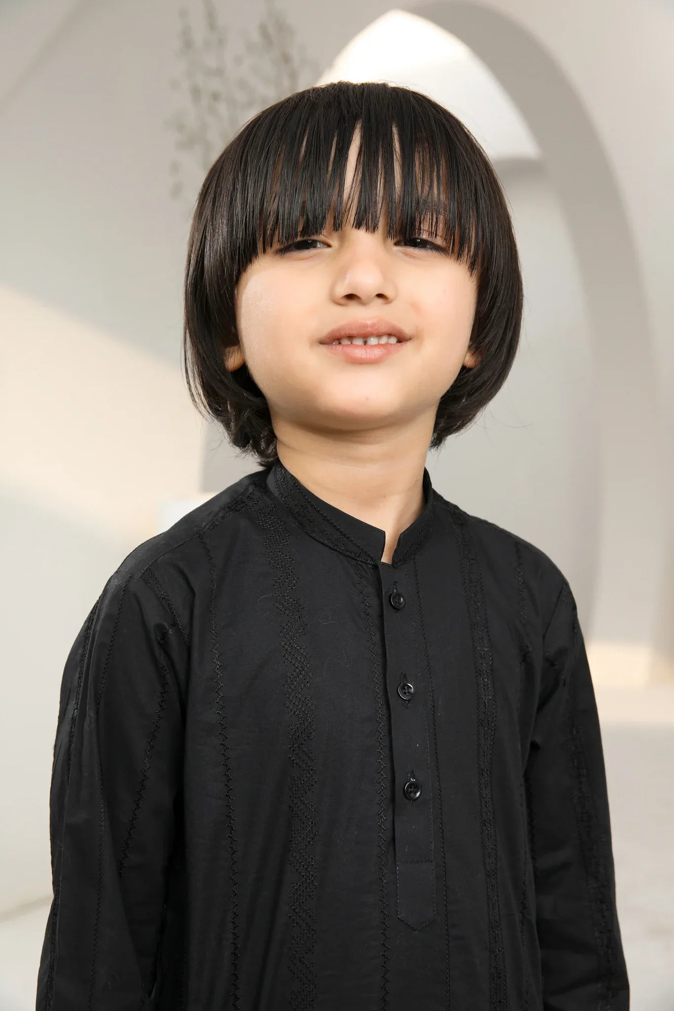 A kid wearing a black traditional embroidered kurta and trouser set.