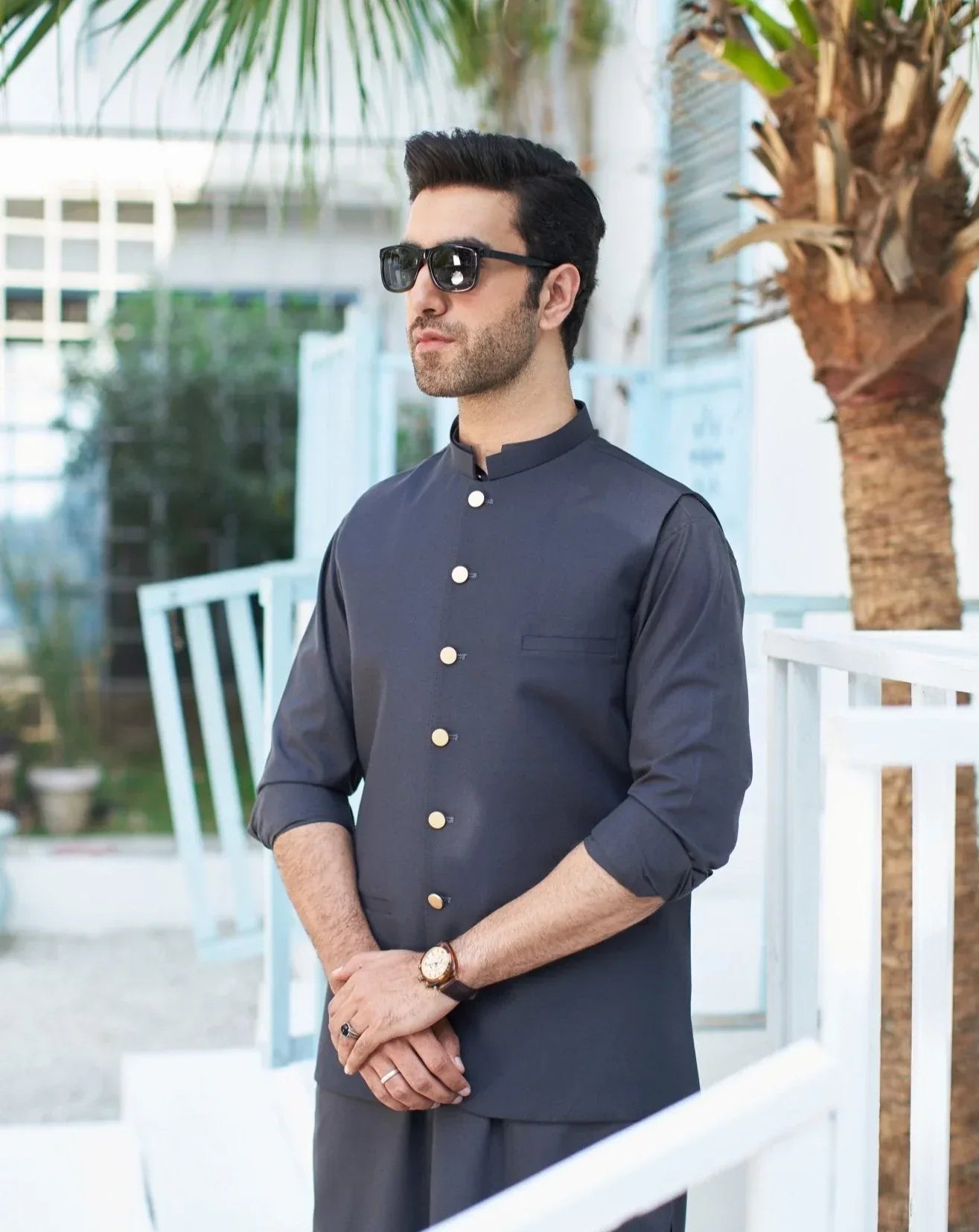 A man standing outside wearing charcoal grey kameez shalwar with waistcoat.