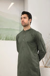 A man standing against a backdrop wearing a army green emnroidered kurta trouser.